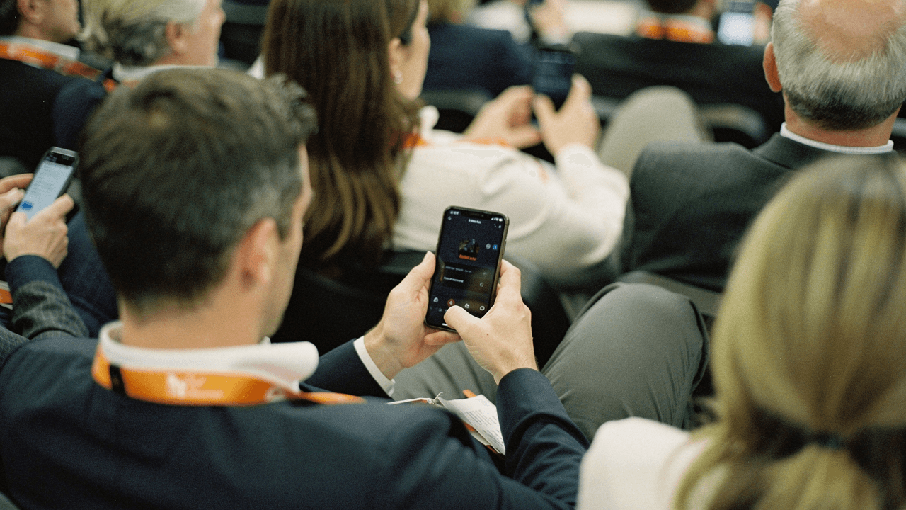 People seated in an audience reading their phones, seen from behind